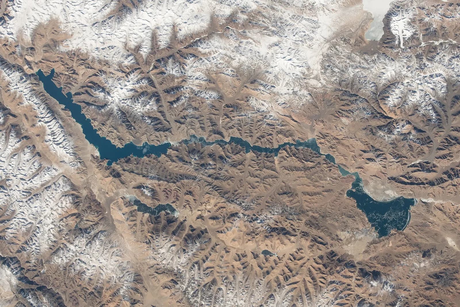 A road curving beside the blue water of Pangong Tso under bare Ladakhi mountains