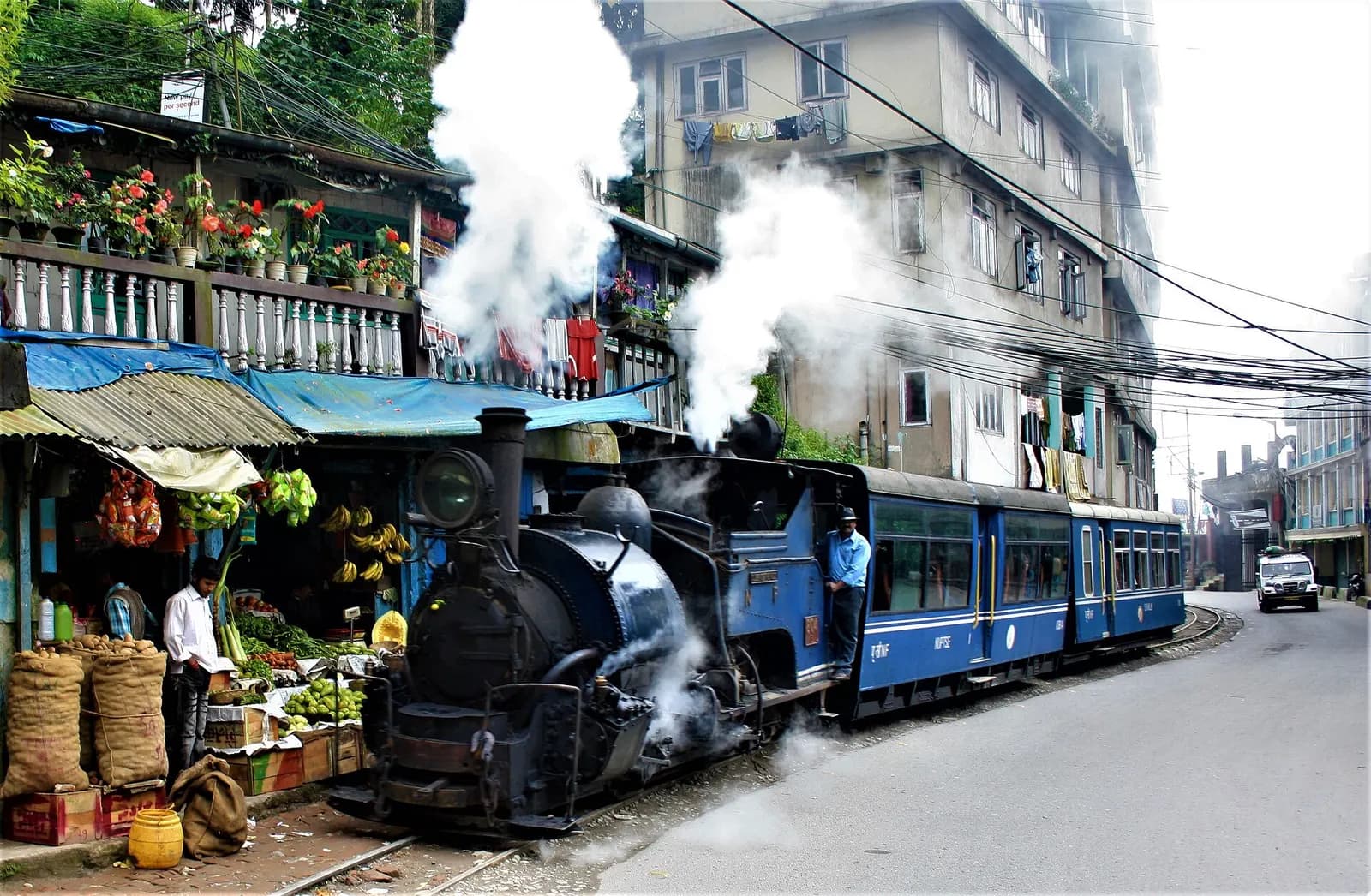 The Darjeeling Himalayan Railway toy train running down a narrow street past shops in Darjeeling