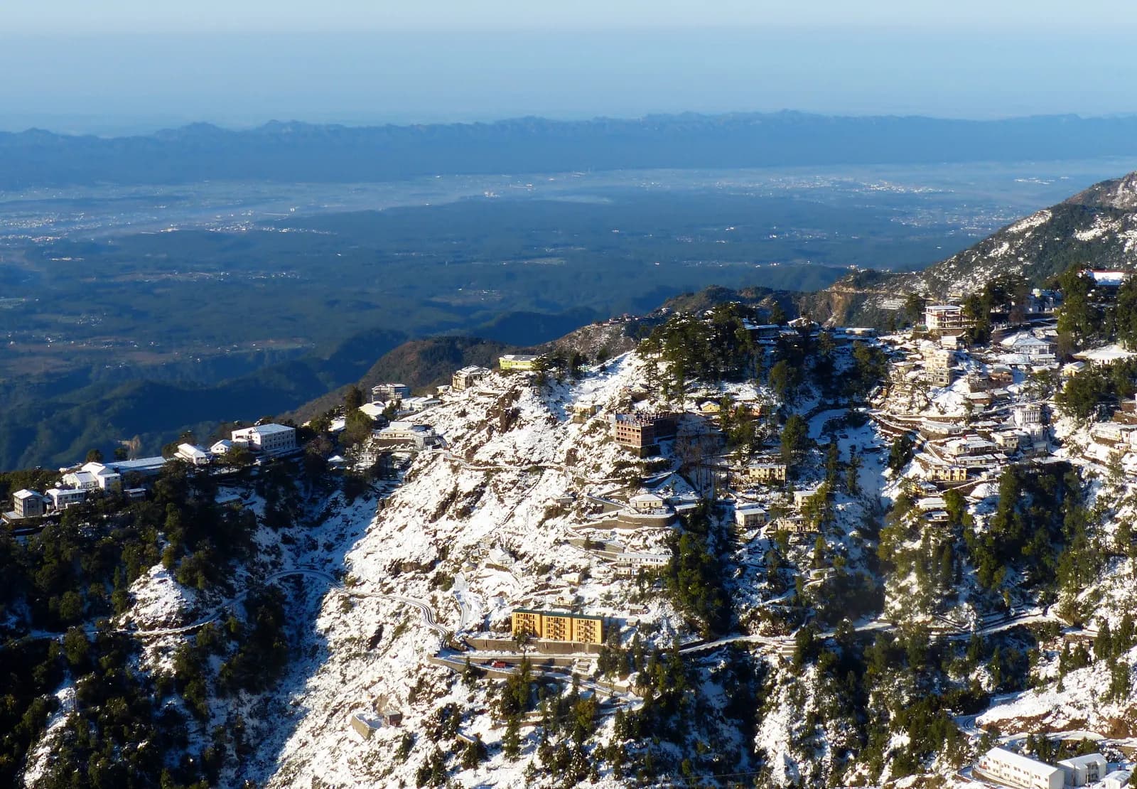 Mussoorie town spread along its ridge with the Doon valley below and the Himalaya behind