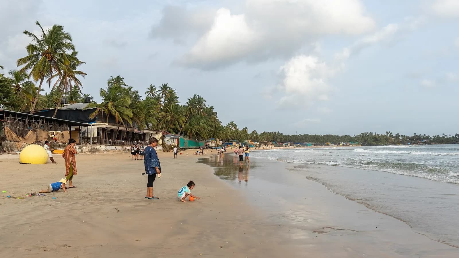 The palm-lined crescent of Palolem beach with wooden huts in South Goa